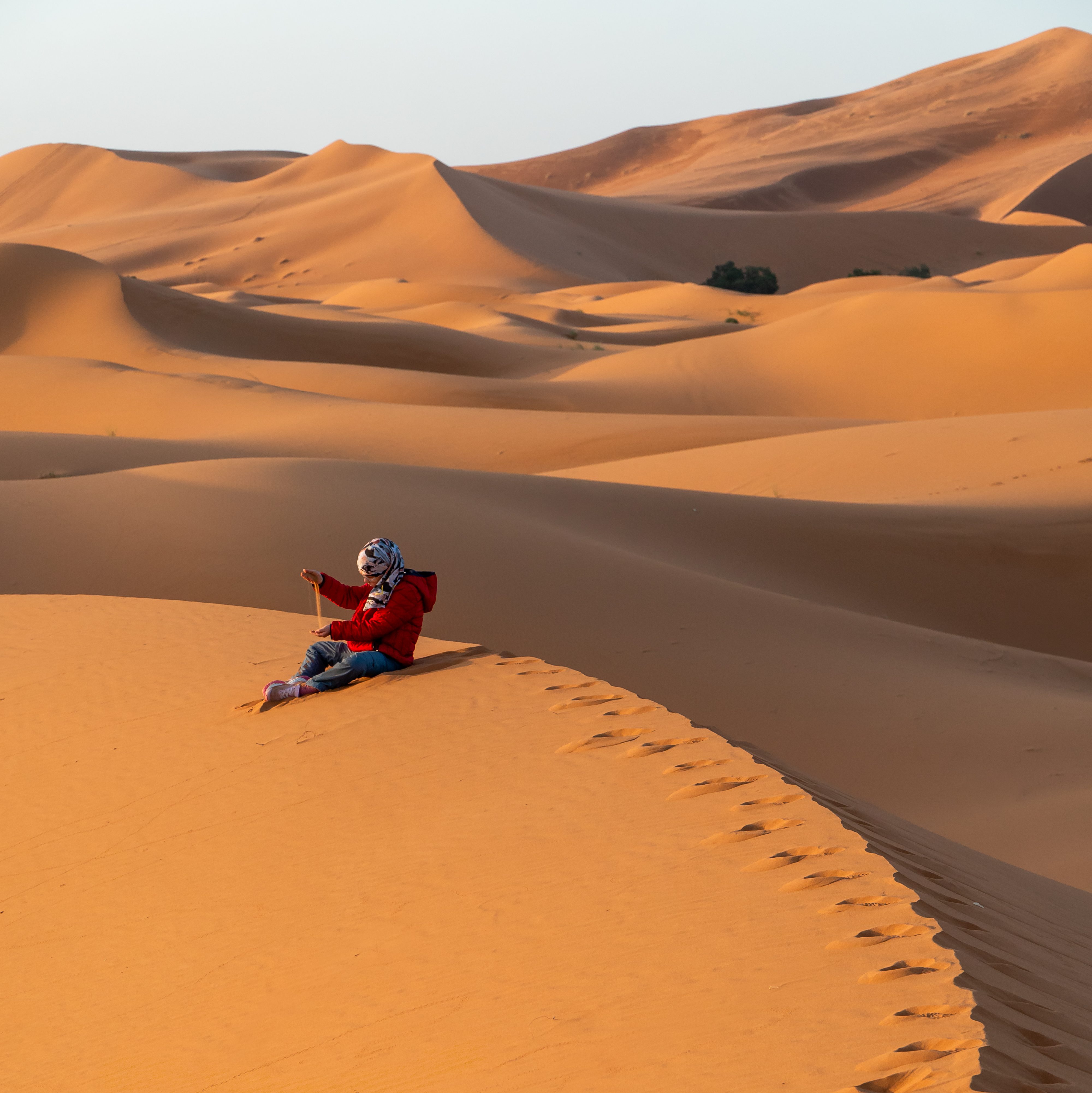 Bambina che gioca con la sabbia sulle dune del deserto dell'Erg Chebbi nei pressi del Riad Ali a Merzouga